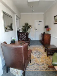 A well lit room with light coloured walls, containing two brown chairs and a round wooden table.